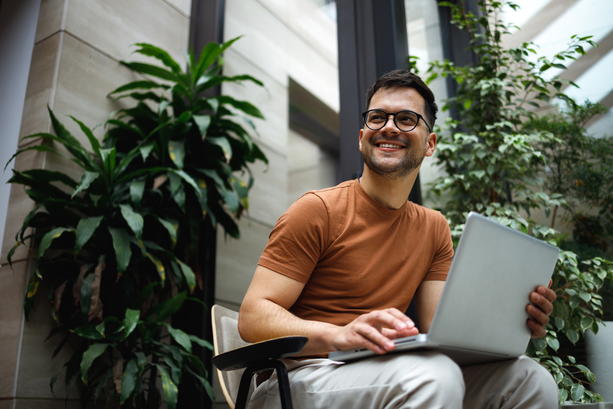 Portrait of a successful young man sitting in the armchair in the modern green building lobby and working on his laptop.