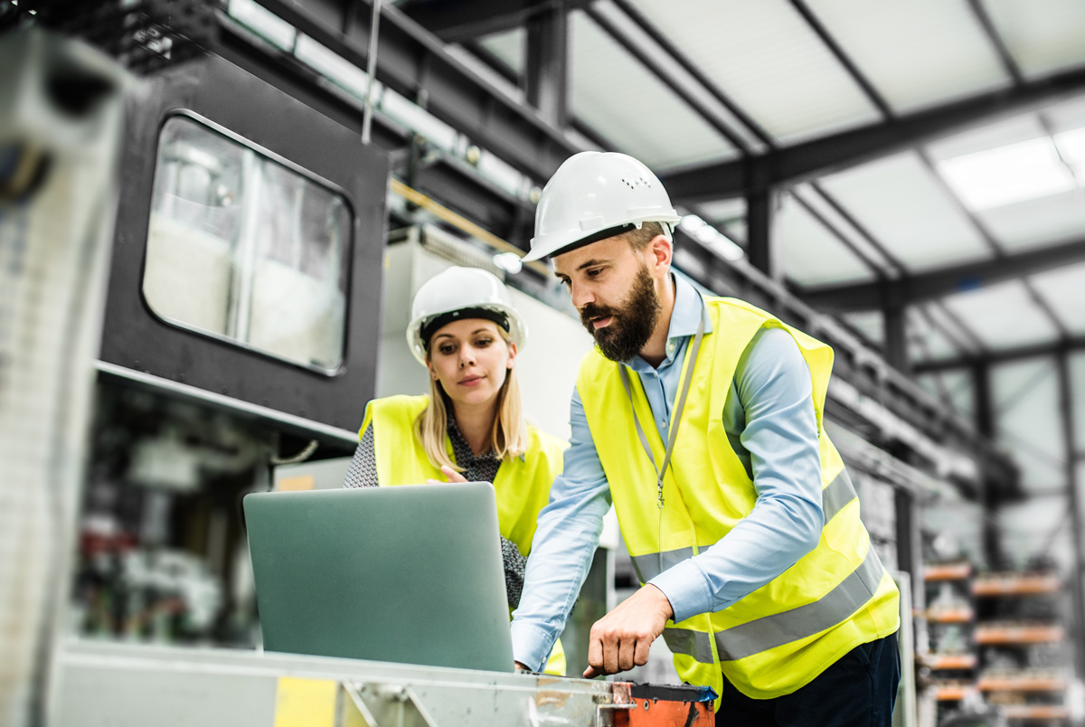 Portrait of a mature industrial man and woman engineer with laptop in a factory, working.